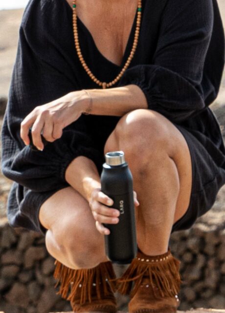 Person in der Hocke hält eine schwarze LARQ Bottle "PureVis" in einer natürlichen, steinigen Landschaft.