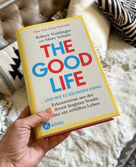 Buch „The Good Life“ von Robert Waldinger und Marc Schulz, in einer Hand gehalten, mit gemütlichem Couch-Hintergrund.