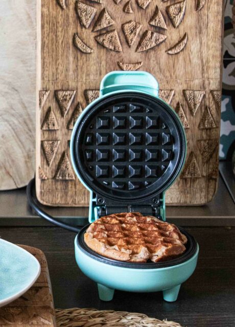 Offenes Mini-Waffeleisen mit einer frisch gebackenen Waffel auf einem rustikalen Holztisch