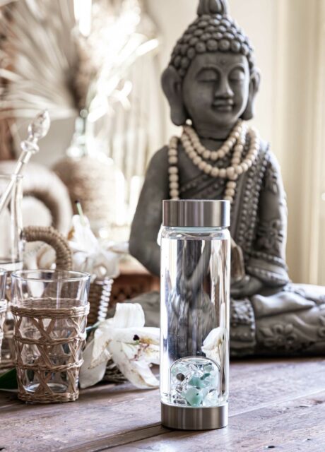 VitaJuwel ViA Edelstein Wasserflasche mit Aquamarin, Aventurin, Rauchquarz und Bergkristall auf einem Boho-Style Holztisch vor einer Buddha-Statue